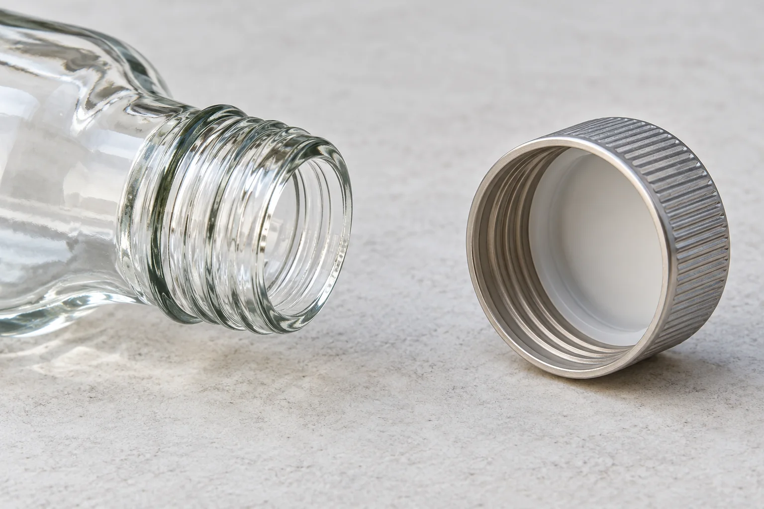 Open glass bottle neck beside a separate closure with its interior visible