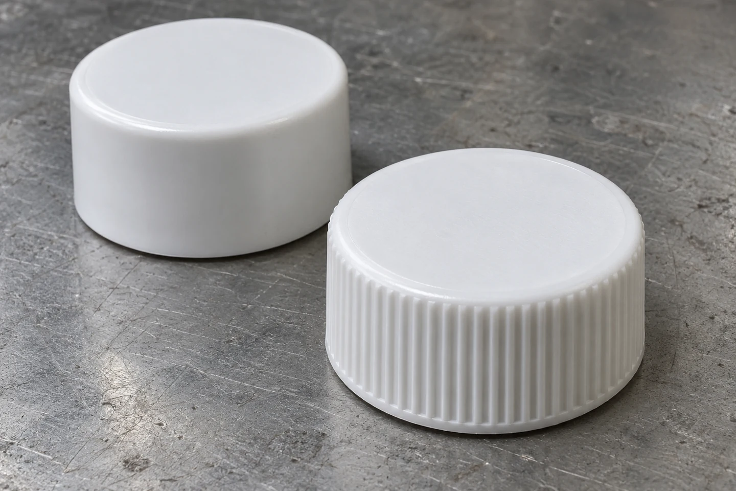 Two white screw caps with a smooth cylindrical skirt at the rear and vertical molded ribs in the foreground